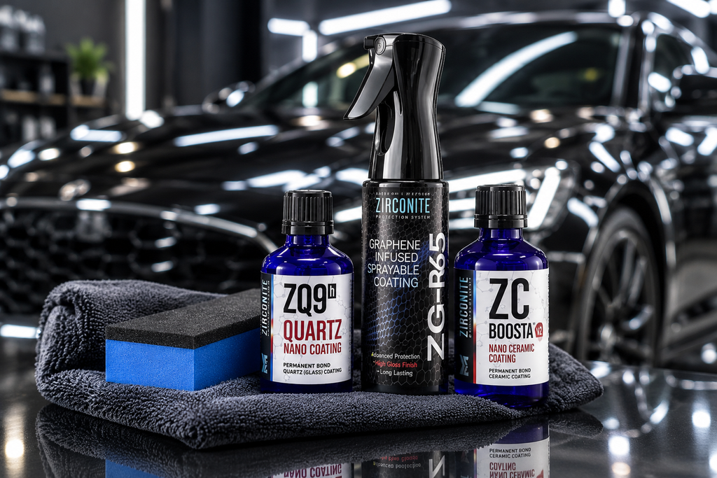 Blue detailing bottles and a spray bottle on a dark towel in a garage, with a glossy black car in the background.